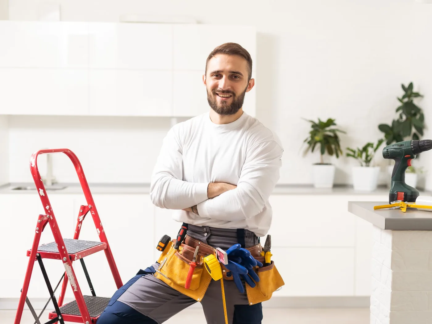 A handyman in a tool belt standing in a bright kitchen