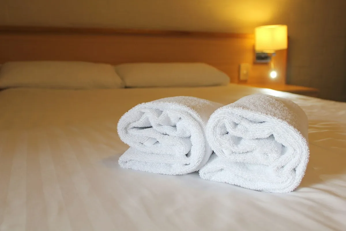 Rolled white towels laid out on a freshly made guest bed
