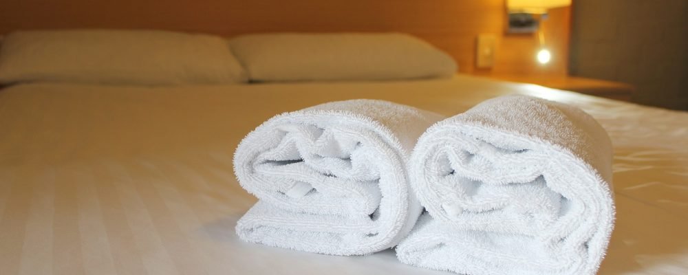 Bedside lamp, pillows and hotel room bed with fresh towels laid out