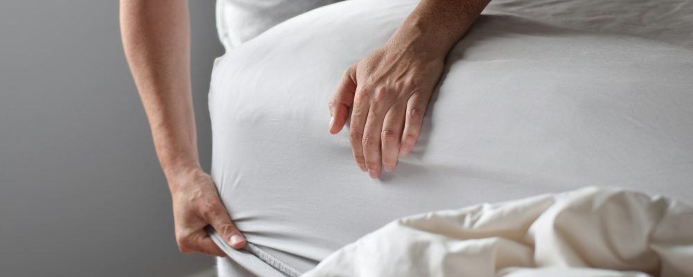 Woman’s hands putting on fitted bed sheet on a mattress while changing bed sheets
